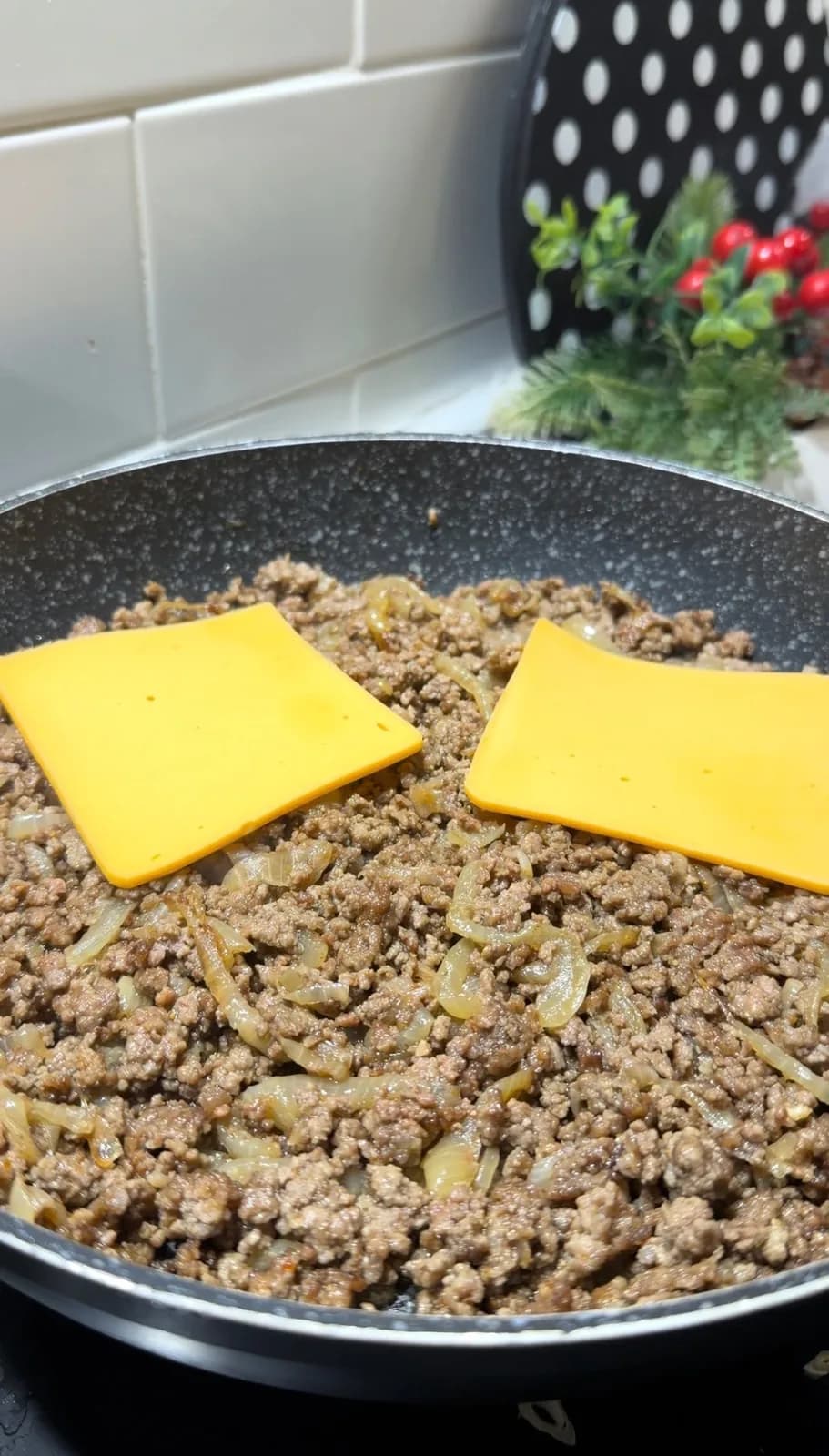 cheddar cheese melting over seasoned ground beef and onions in a pan
