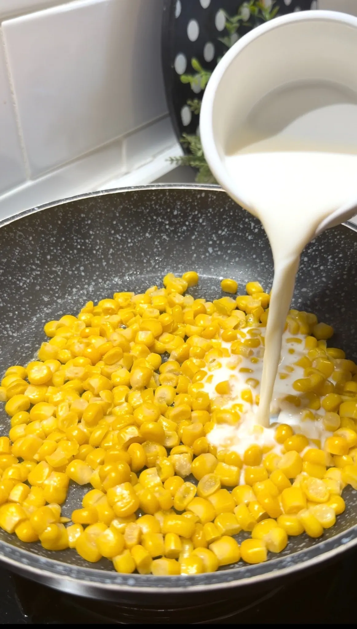 Milk being poured over corn while making cheesy corn dip