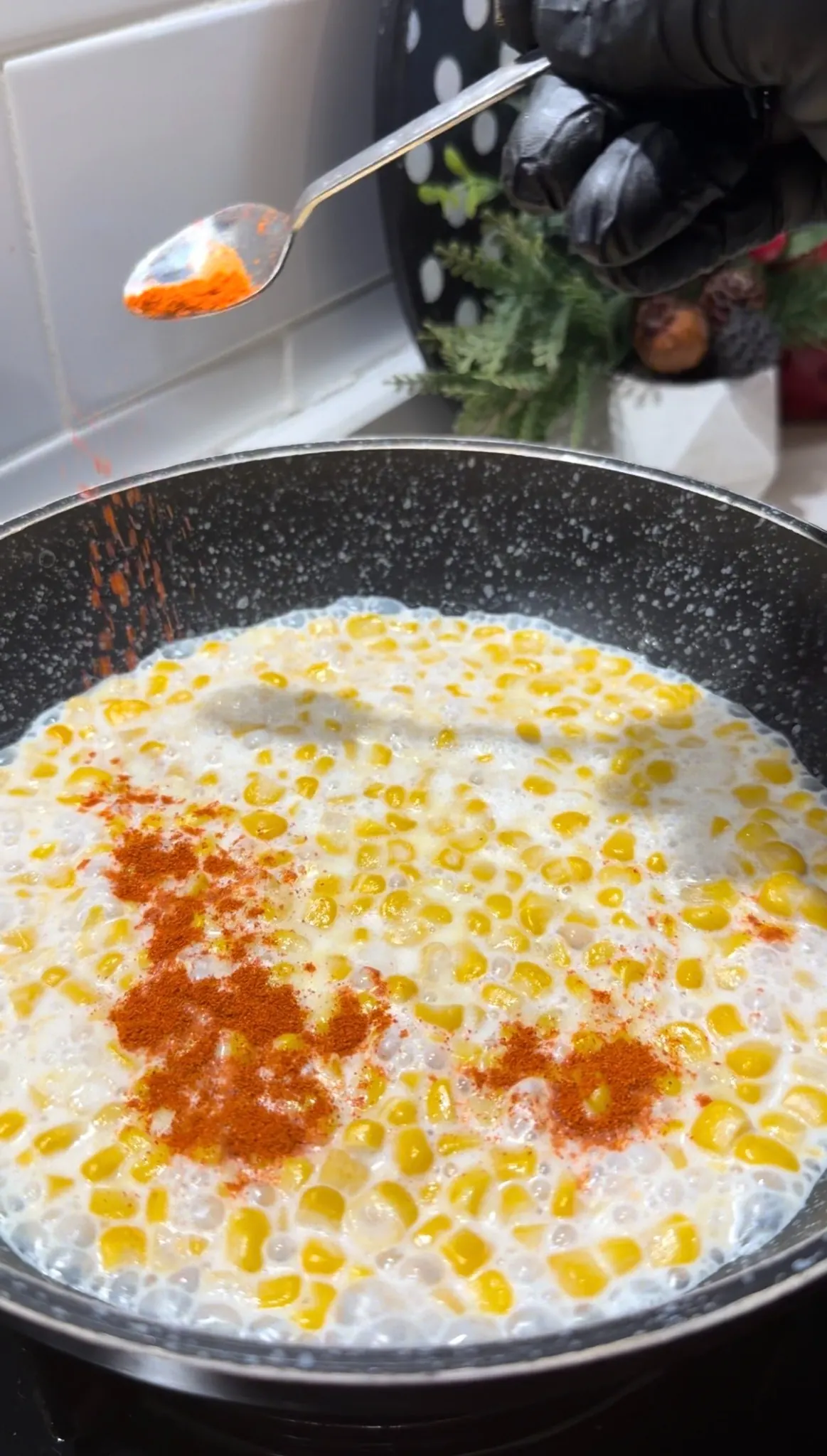 Ground red pepper being added to creamy corn in a skillet