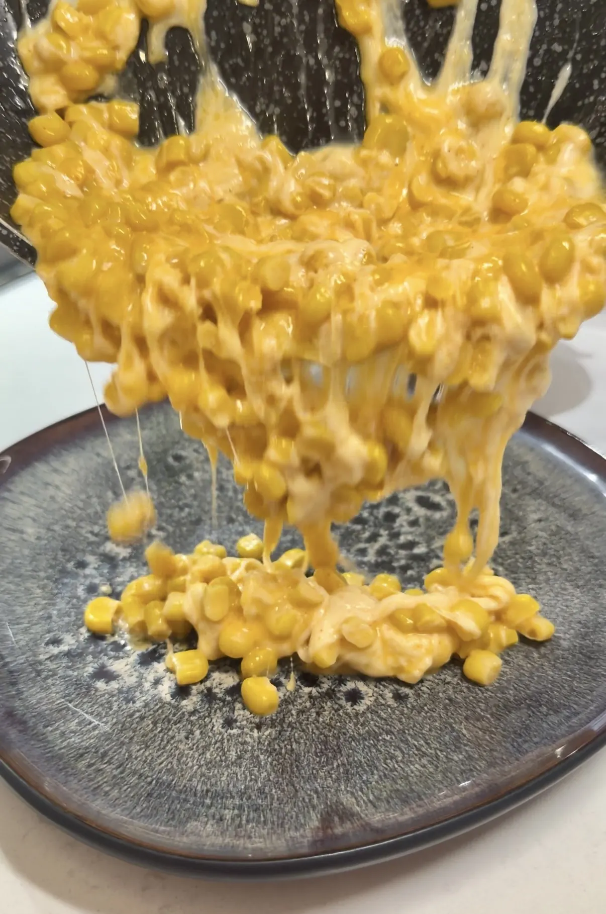 Creamy cheesy corn dip with melted cheese stretching from the skillet
