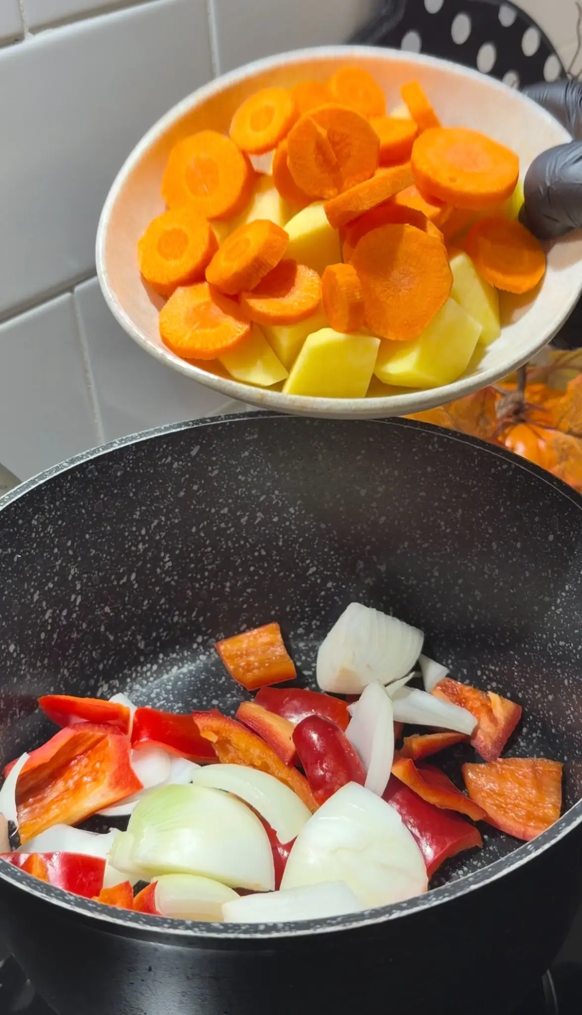 Chopped potatoes and sliced carrots being added to onion and red bell pepper in a pot