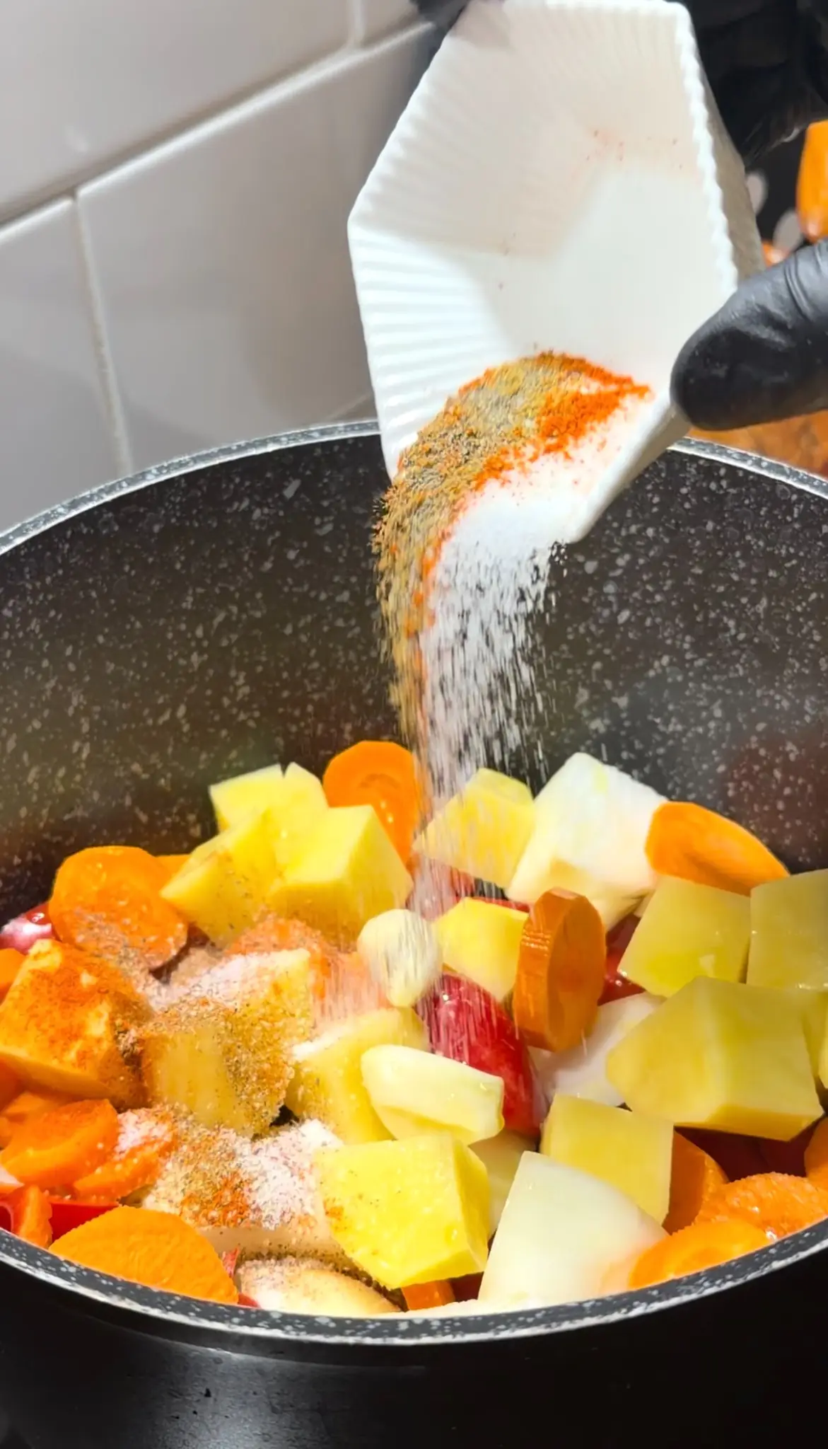 Salt, black pepper, cumin, and sweet paprika being added to vegetables in a soup pot