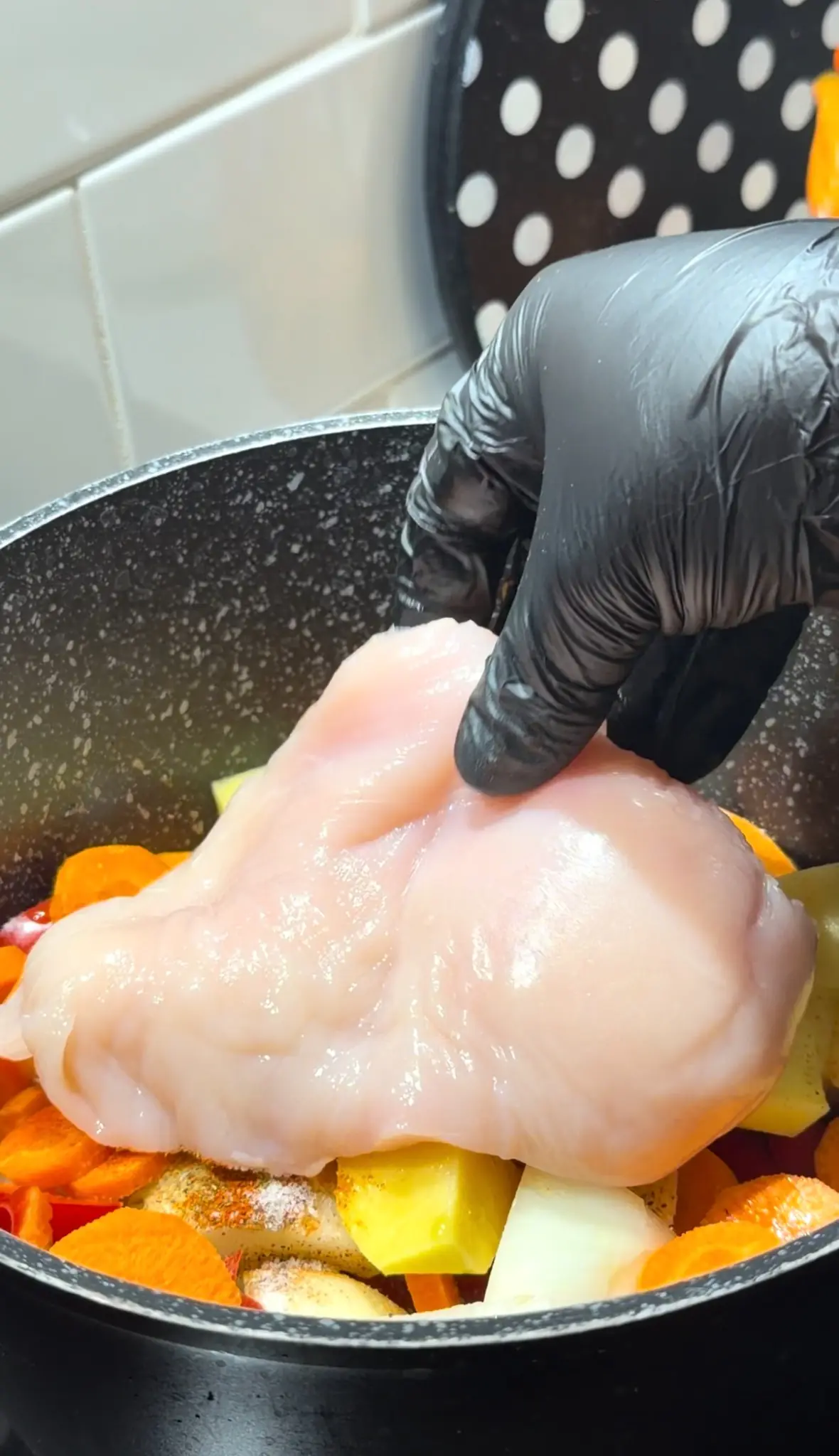 Raw chicken breast being placed over seasoned vegetables in a pot