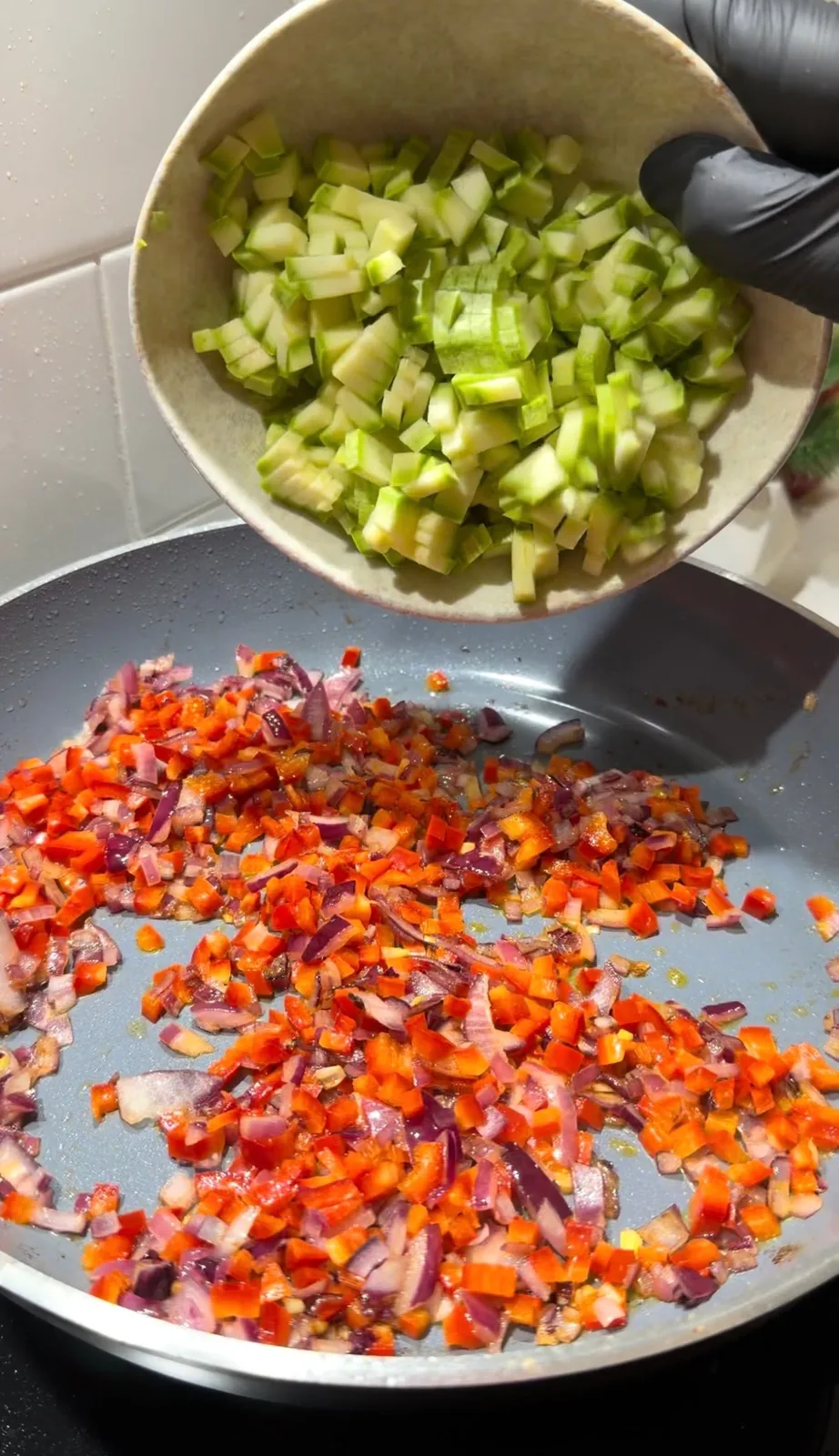 chopped zucchini being added to sautéed red onion and red pepper in a pan