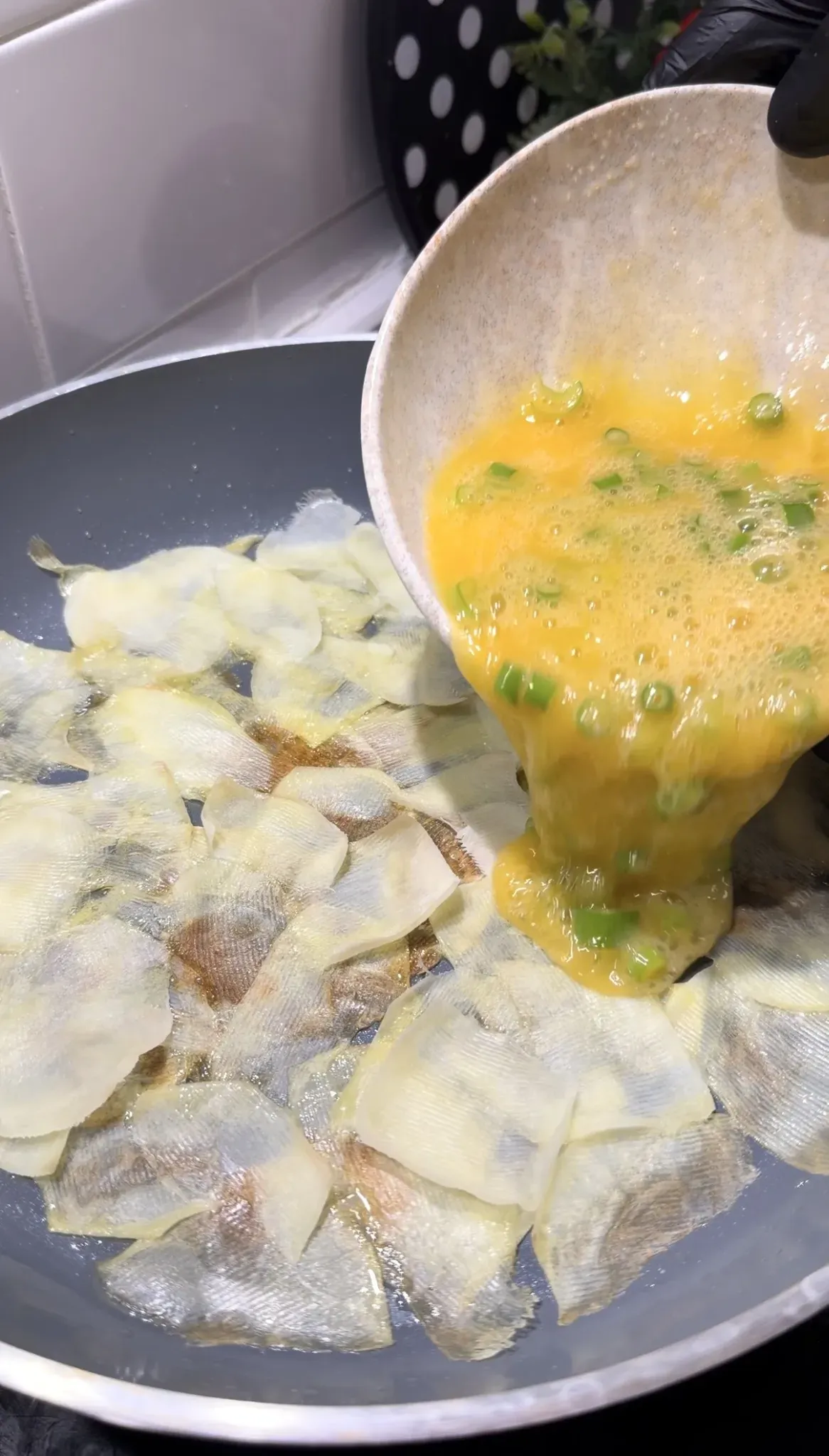 Thin potato slices cooking in olive oil in a non-stick pan