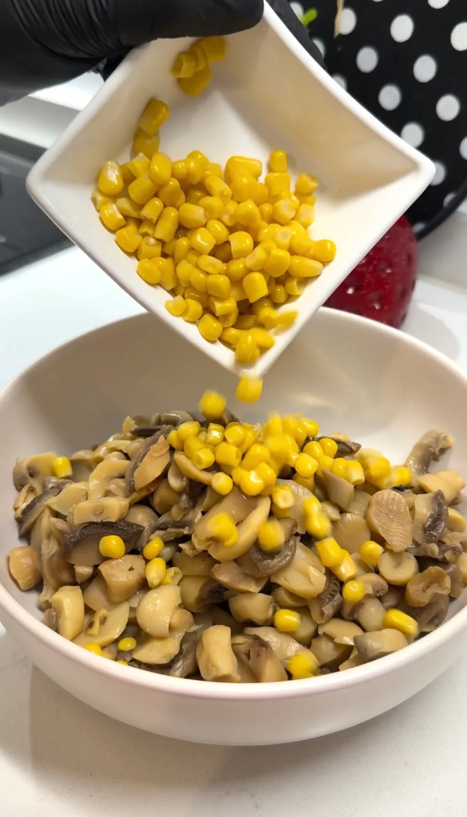 canned corn being added to drained pickled mushrooms for an easy mushroom salad