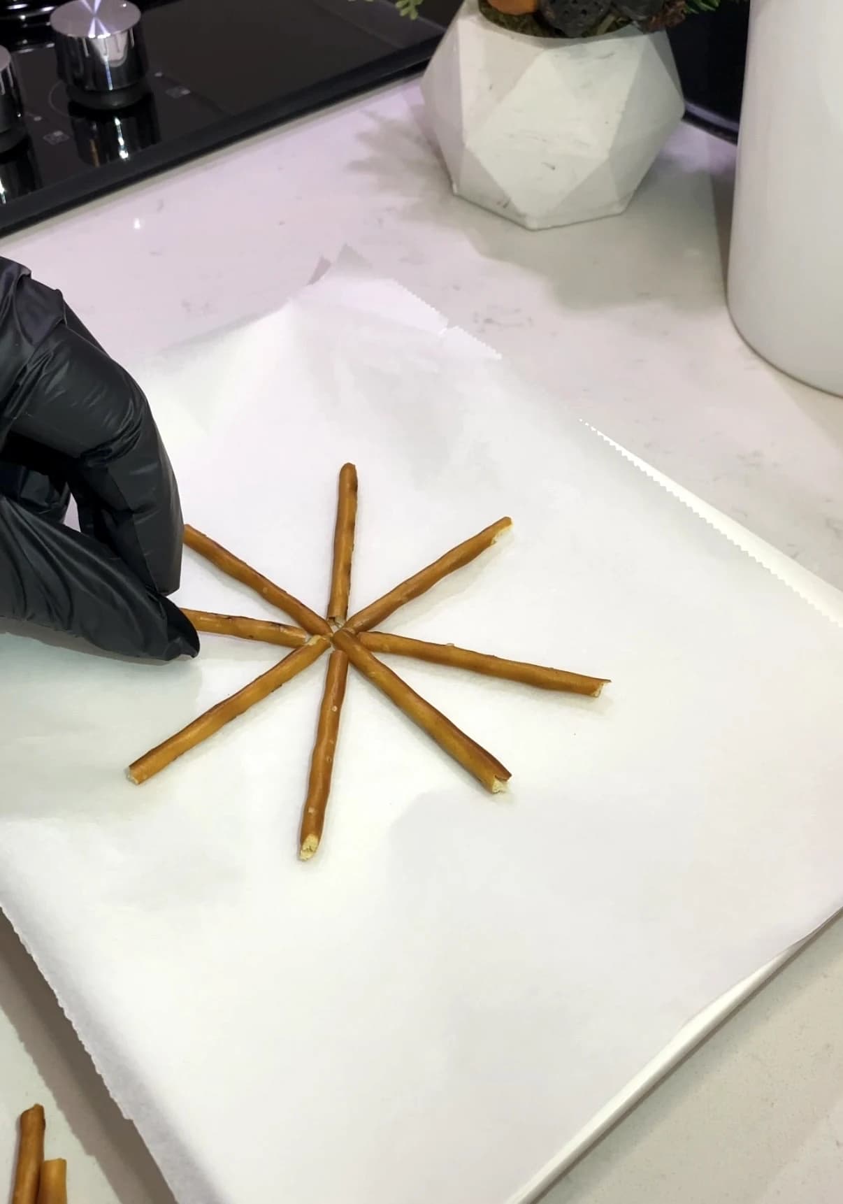 Pretzel sticks arranged in a spider web shape on parchment paper