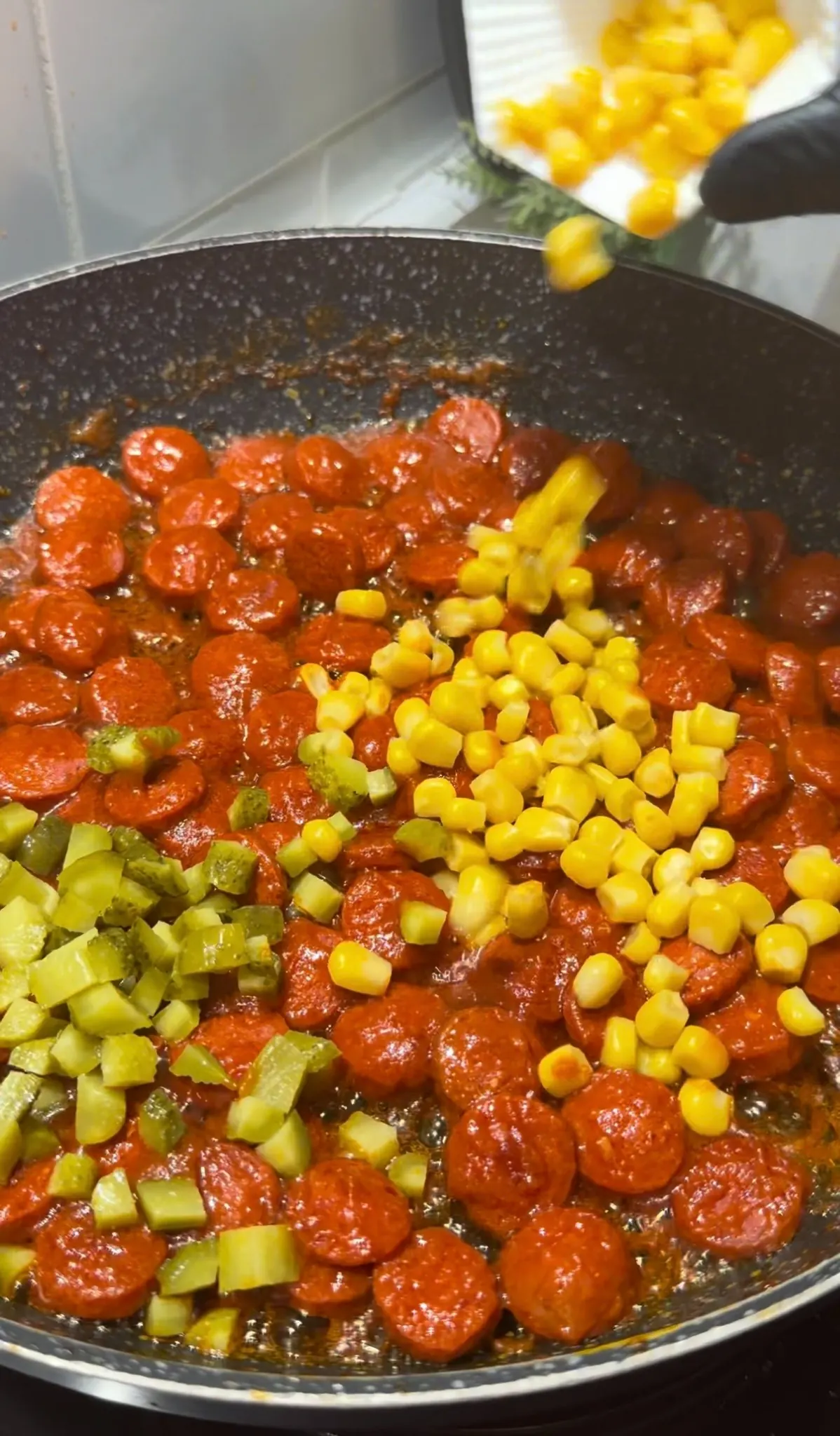 Chopped pickles and corn being added to saucy beef sausages