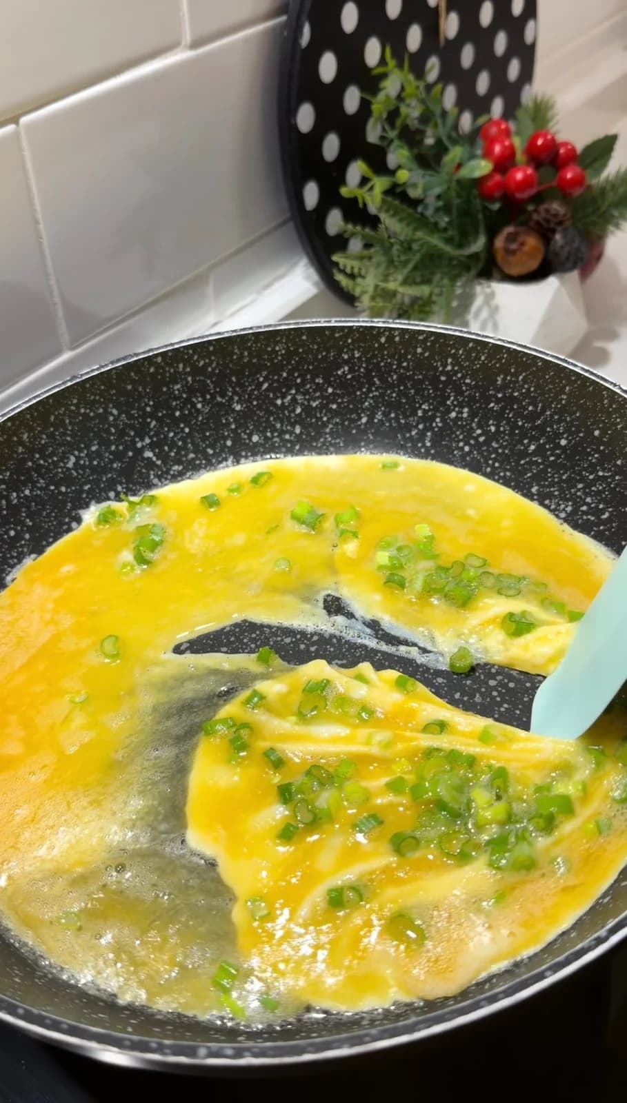 Thin layer of egg and green onions cooking in a pan for Japanese rolled omelette