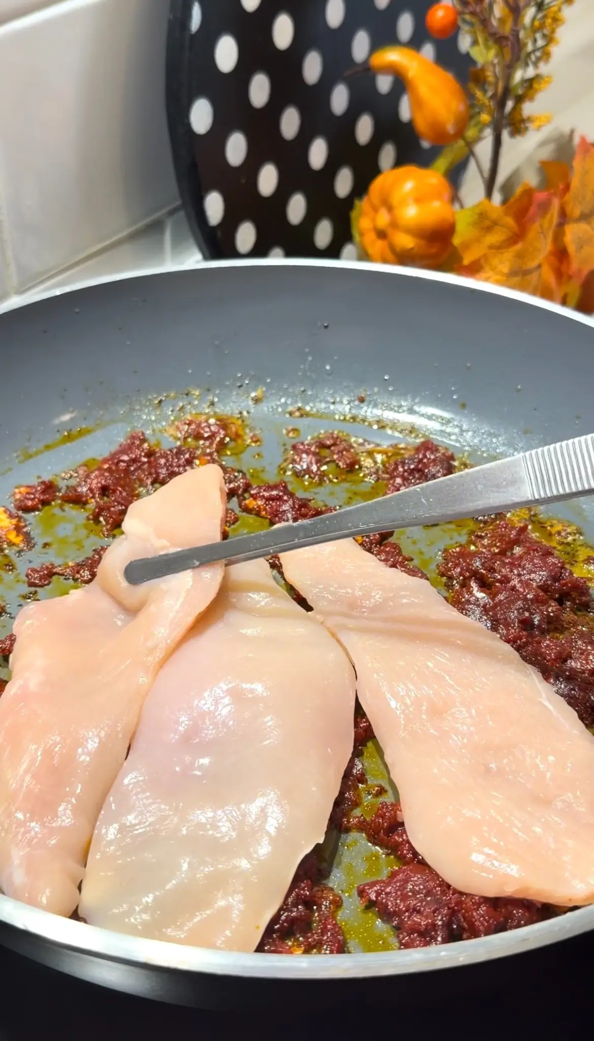 Raw chicken breast fillets being added to seasoned tomato paste in a skillet