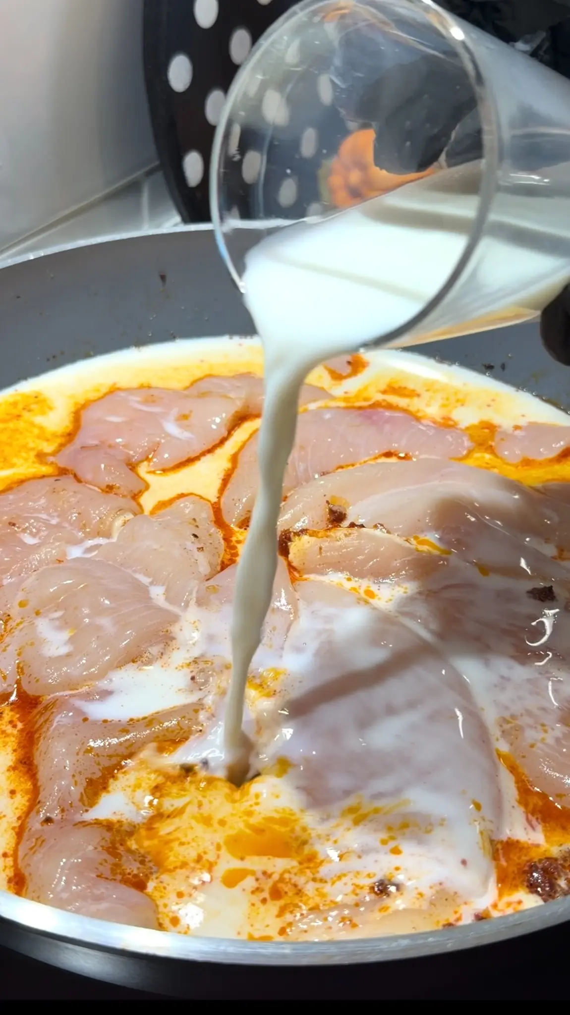 Room-temperature milk being poured over chicken breast and tomato sauce
