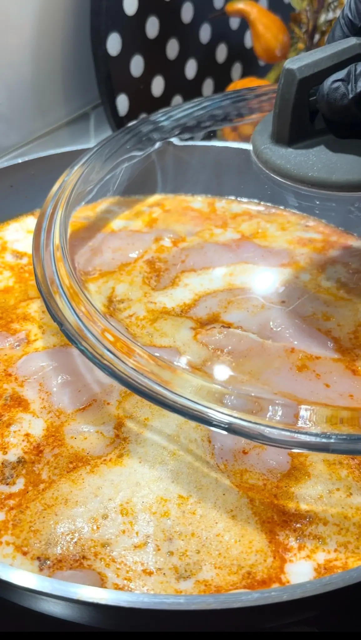 Chicken breast simmering in milk and sparkling mineral water under a covered skillet