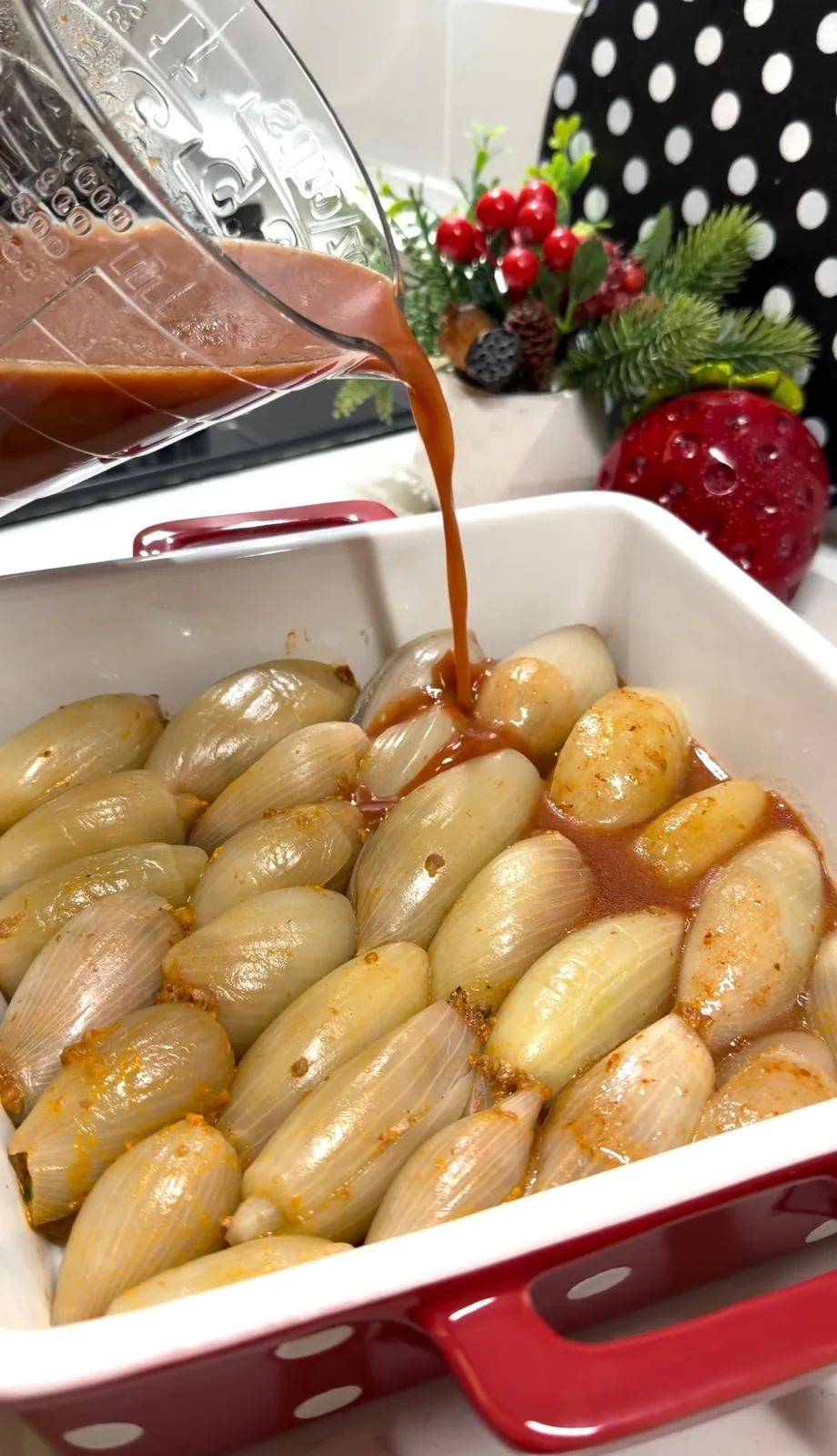tomato and pomegranate sauce being poured over stuffed onions before baking