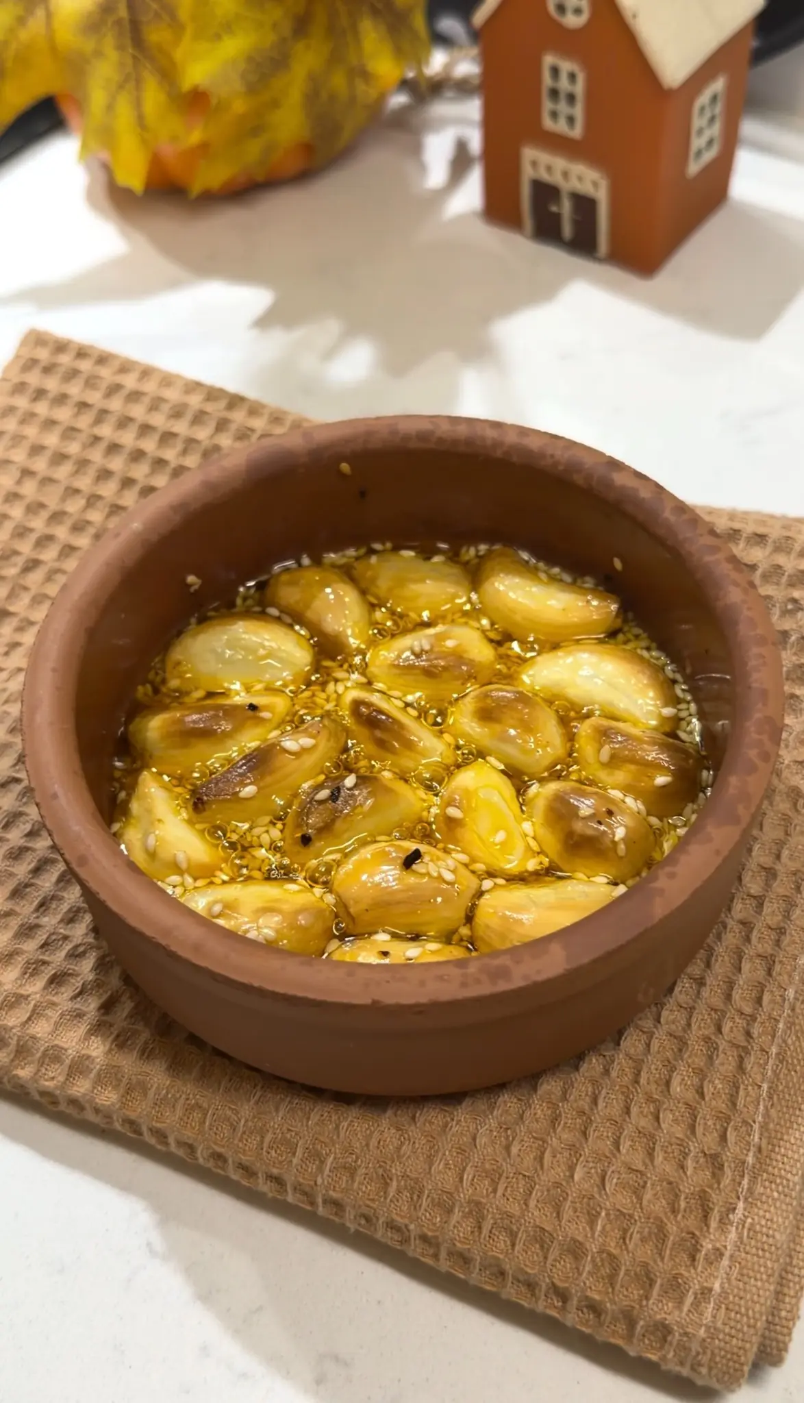 Golden roasted garlic cloves with sesame seeds and olive oil in a small baking dish.