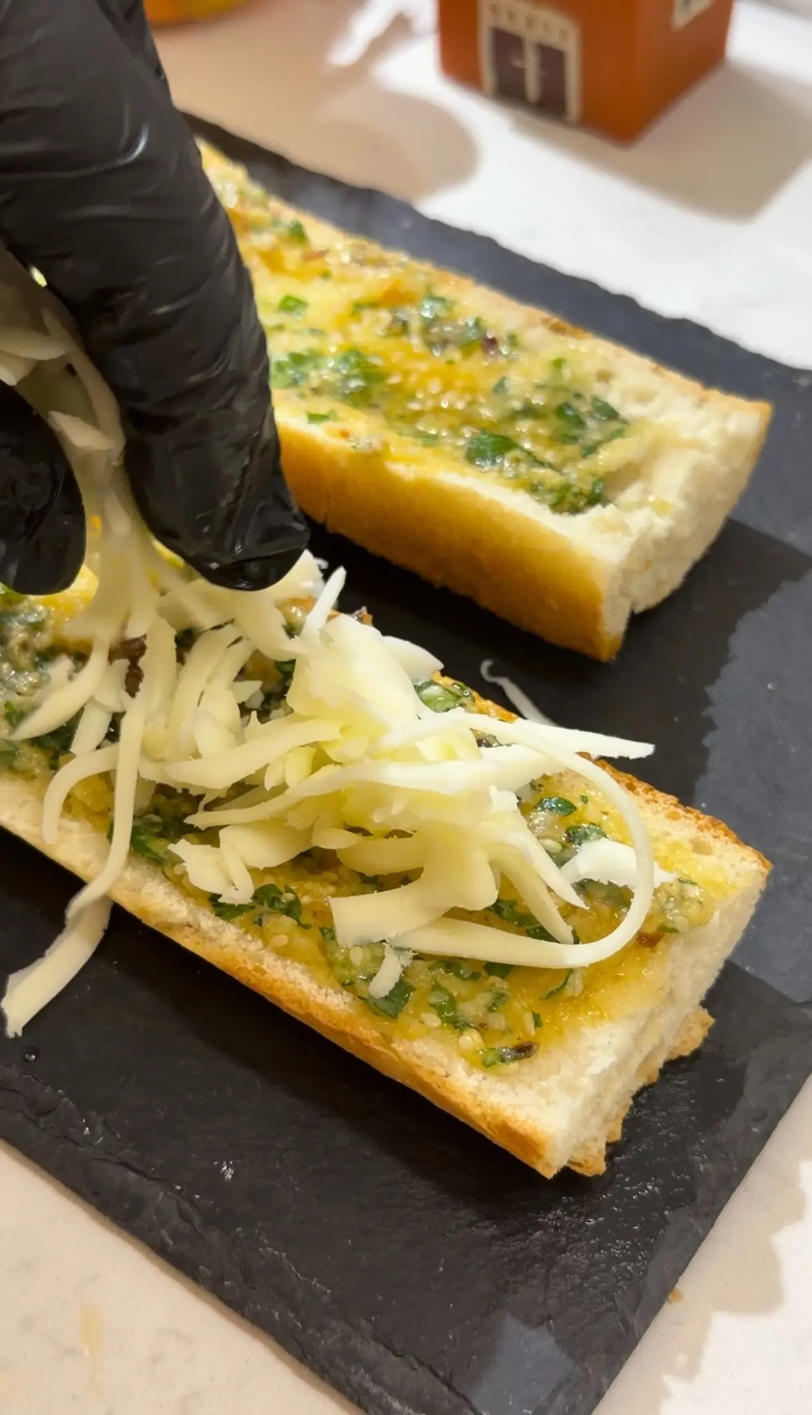 Adding grated fresh kaşar cheese to bread spread with roasted garlic butter.