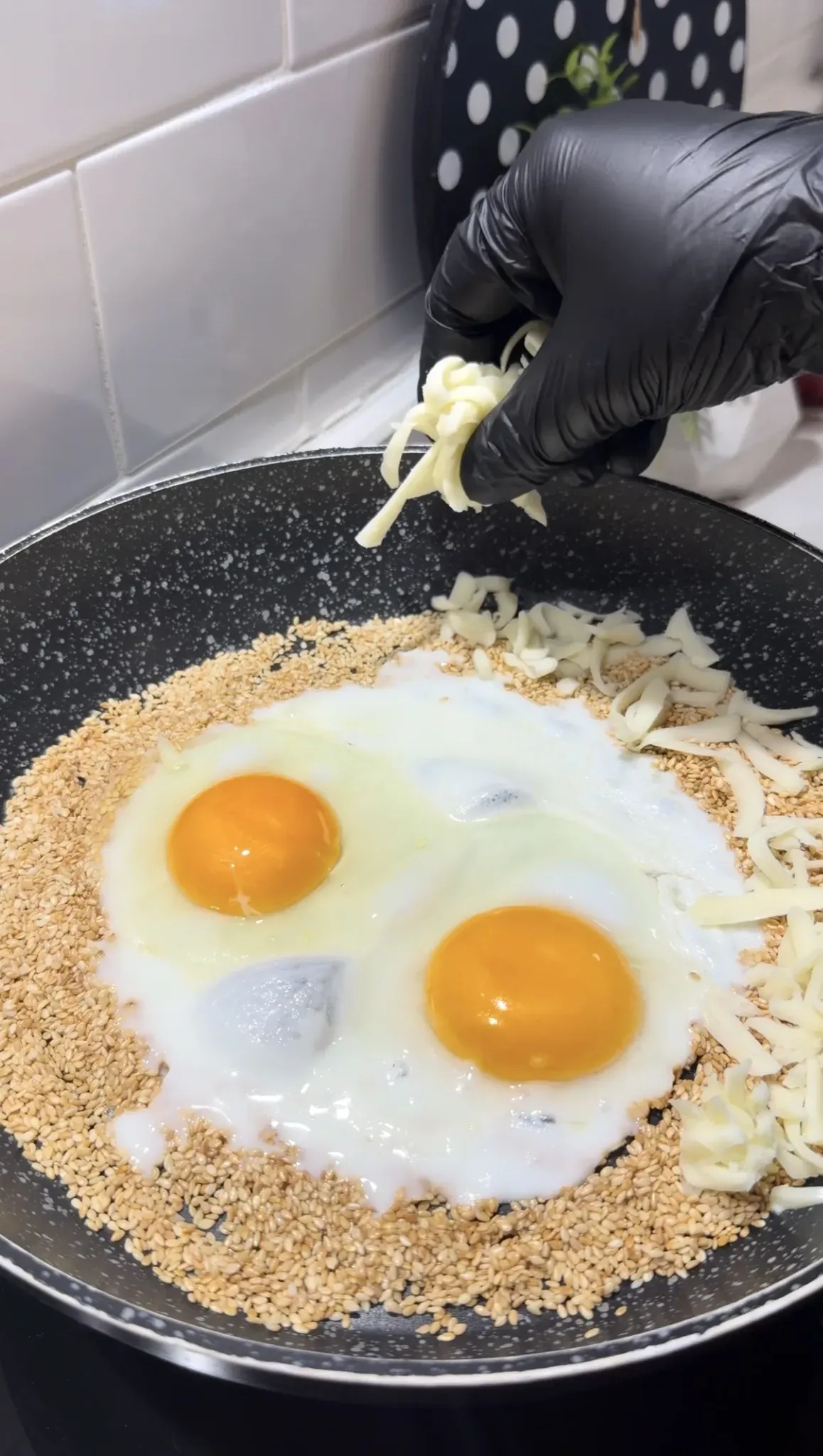Eggs and grated cheese cooking over toasted sesame seeds in a pan