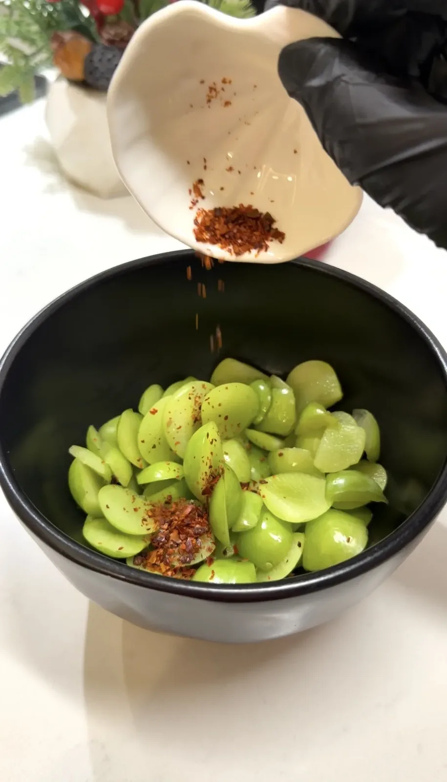 sumac and chili flakes being sprinkled over sliced green plums