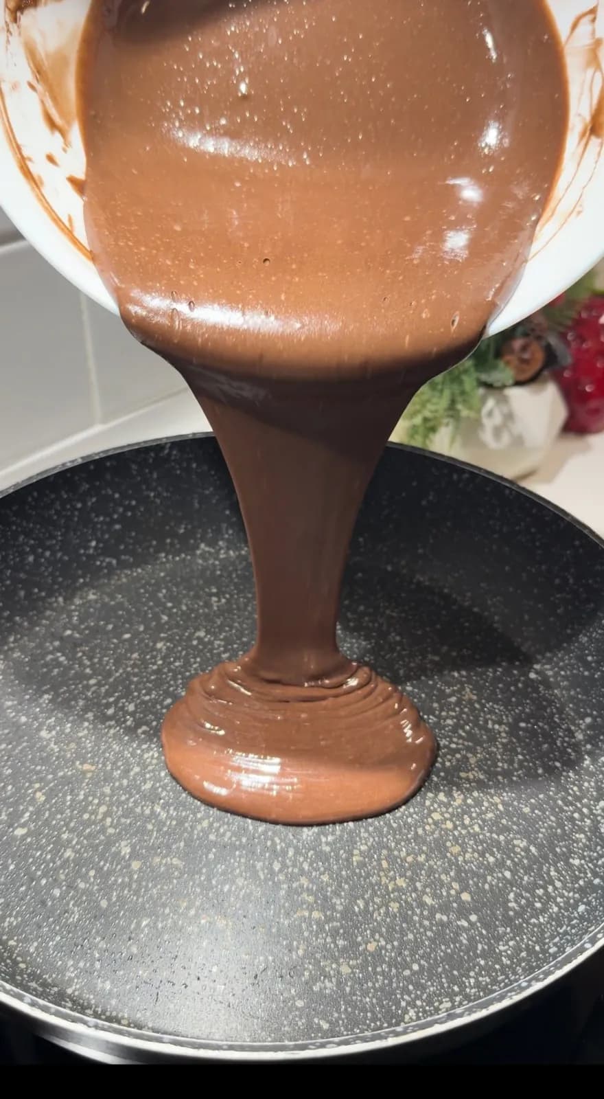 Chocolate pancake batter being poured into a non-stick pan