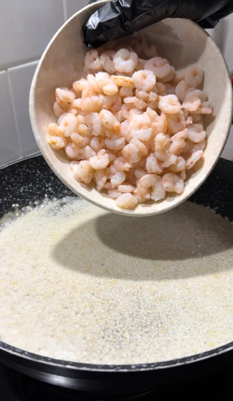 Cooked shrimp being added to a pan with toasted sesame seeds