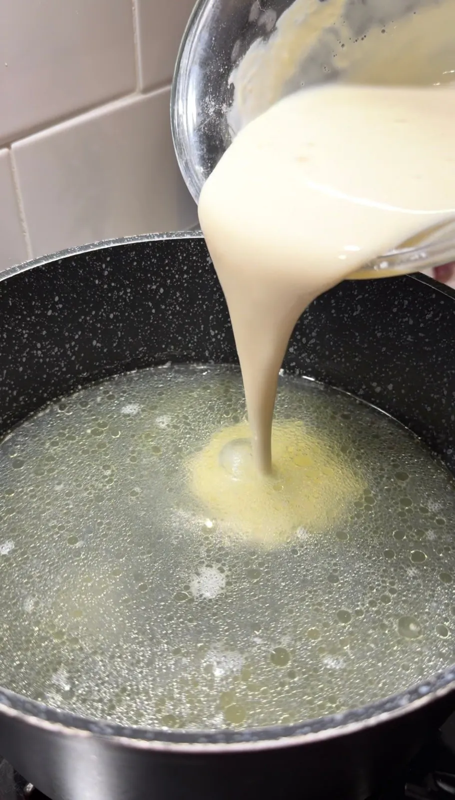 Hot chicken broth being slowly added to yogurt mixture to prevent curdling