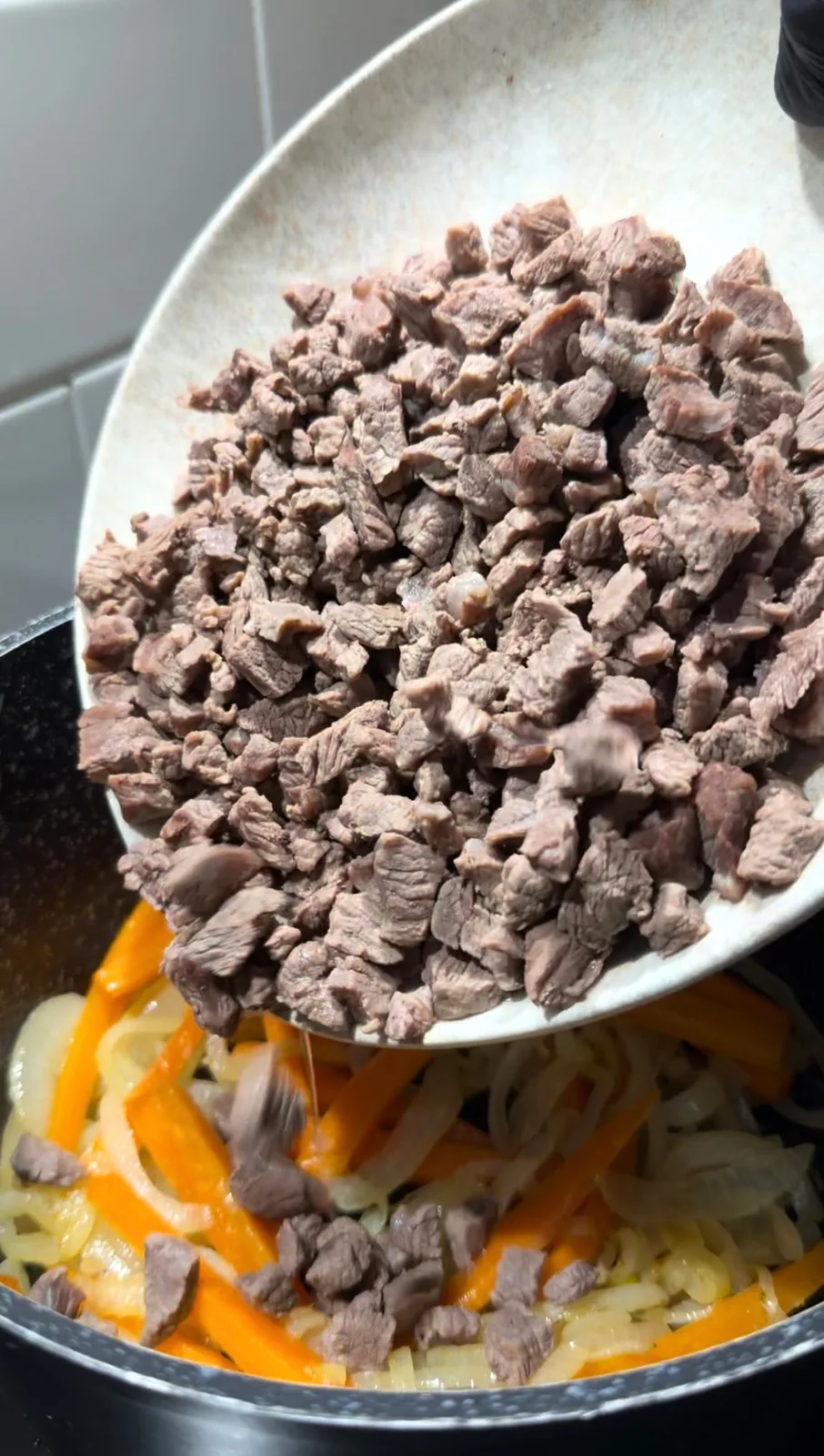 cubed beef being added to sautéed onions and carrots for Uzbek pilaf