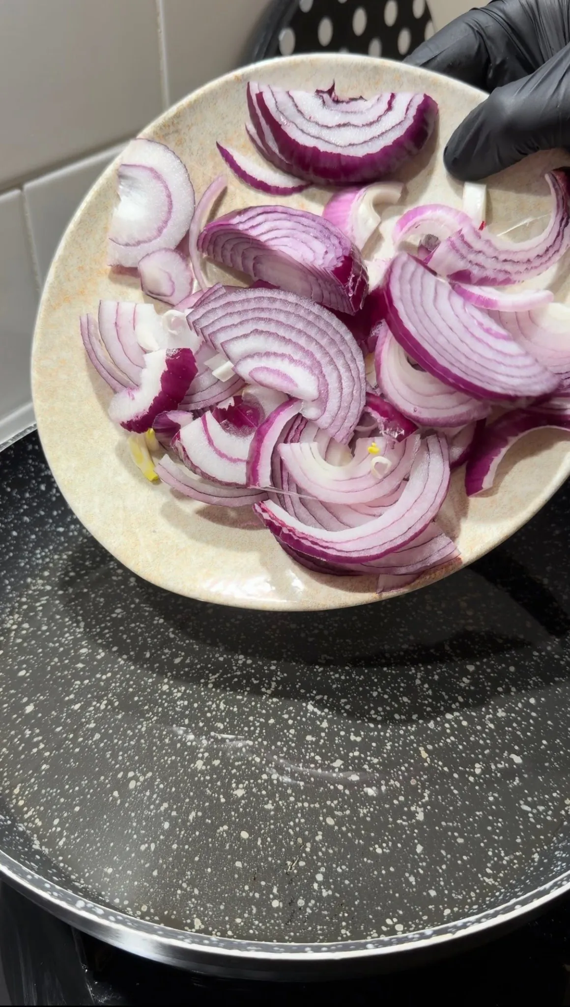 Sliced red onions being added to a pan for Turkish yogurt onion sauté