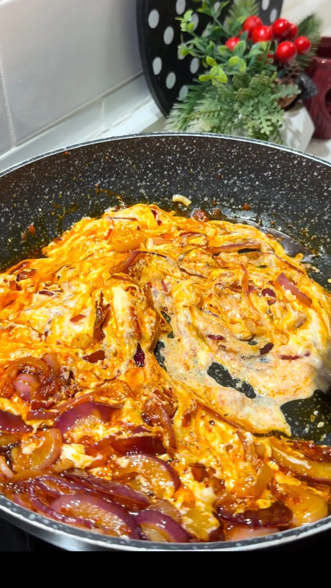 Yogurt mixed with caramelized red onions and spices in a pan